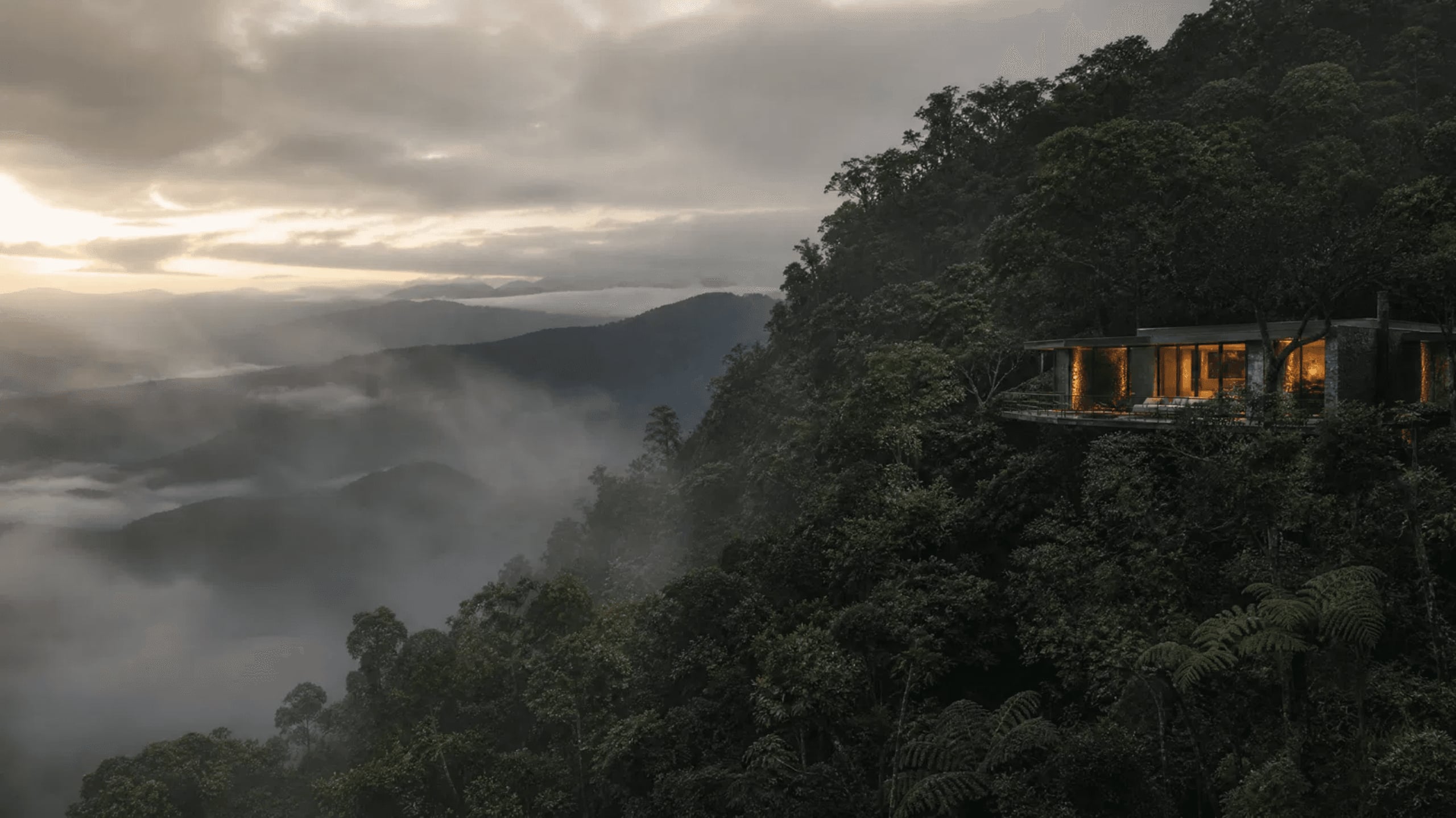 Suíte de vidro e pedra suspensa sobre a mata da Serra da Mantiqueira ao amanhecer, acima do mar de nuvens